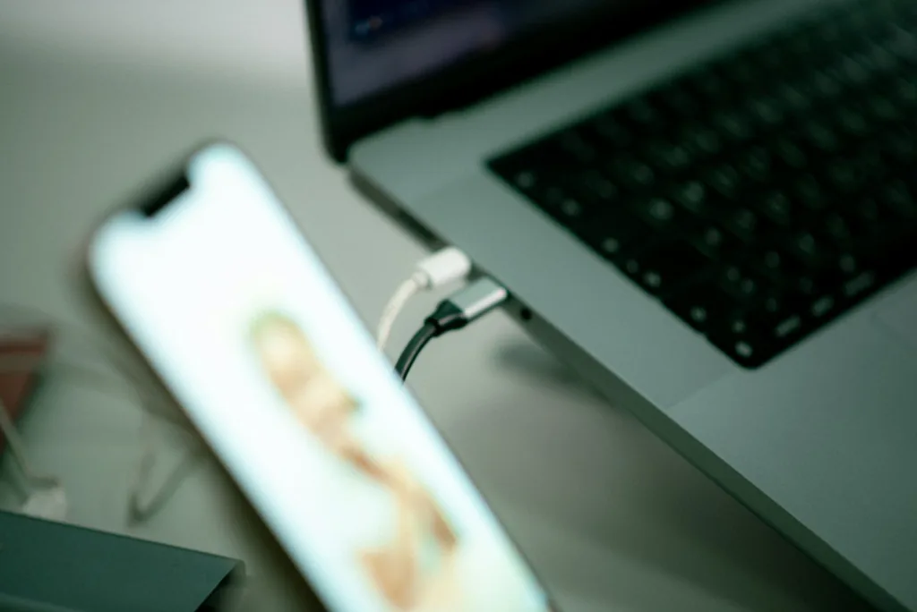 Smartphone connected to a laptop by a charging cable on a desk.