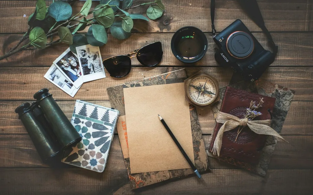 Travel flat lay of a camera, binoculars, compass, instant photos and notebook.