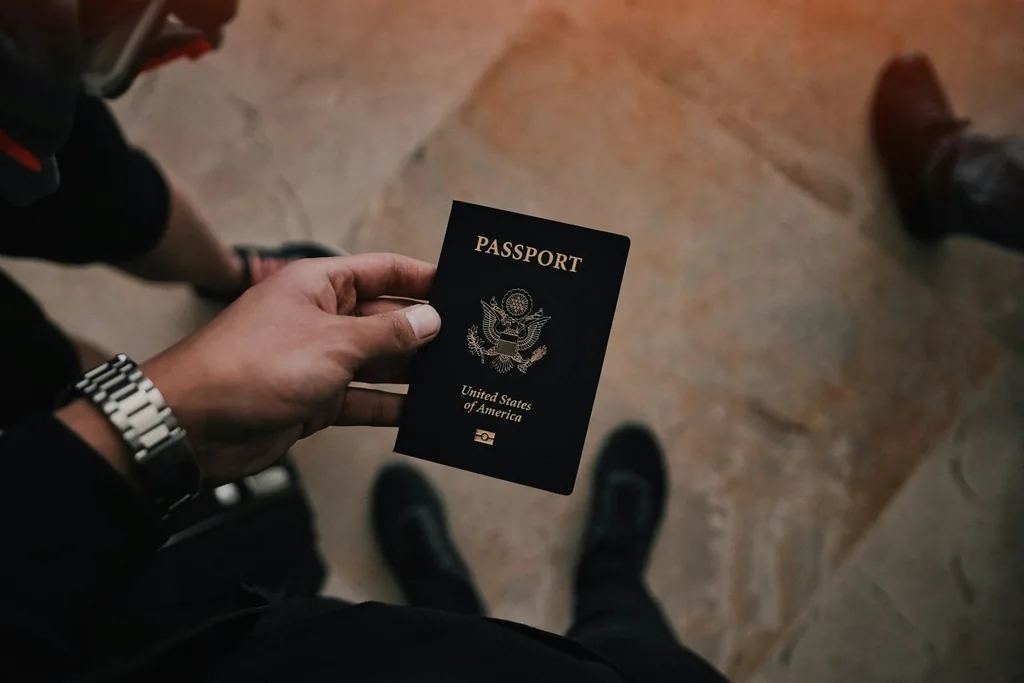 A hand holds a dark blue passport with gold lettering above a stone floor.