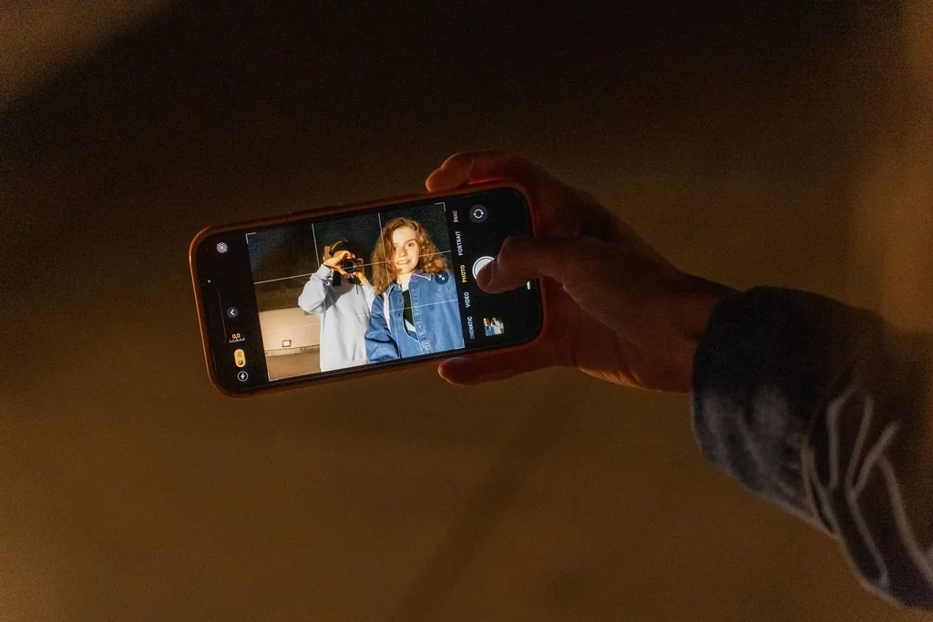 A hand holds a phone up in a dark, amber-lit room, its camera framing two friends.