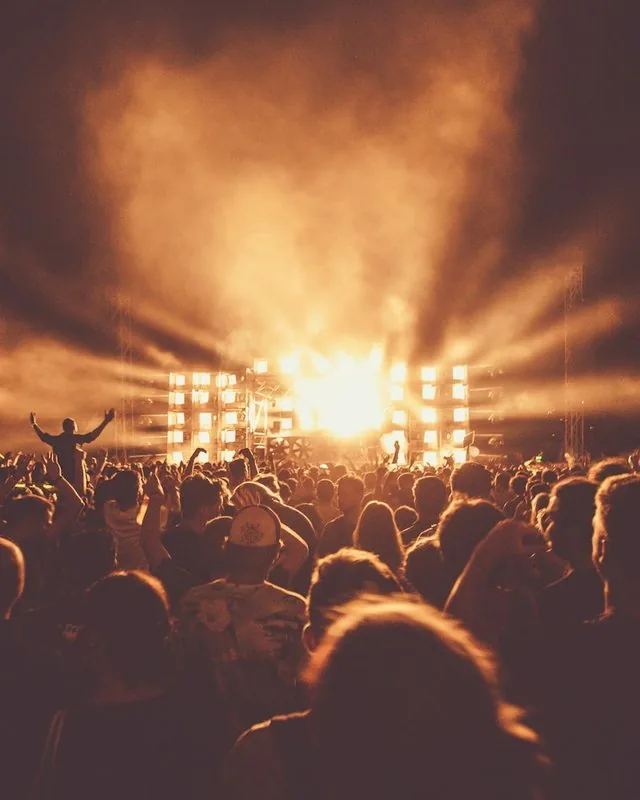 Crowd silhouetted before a concert stage blazing with amber lights and smoke.